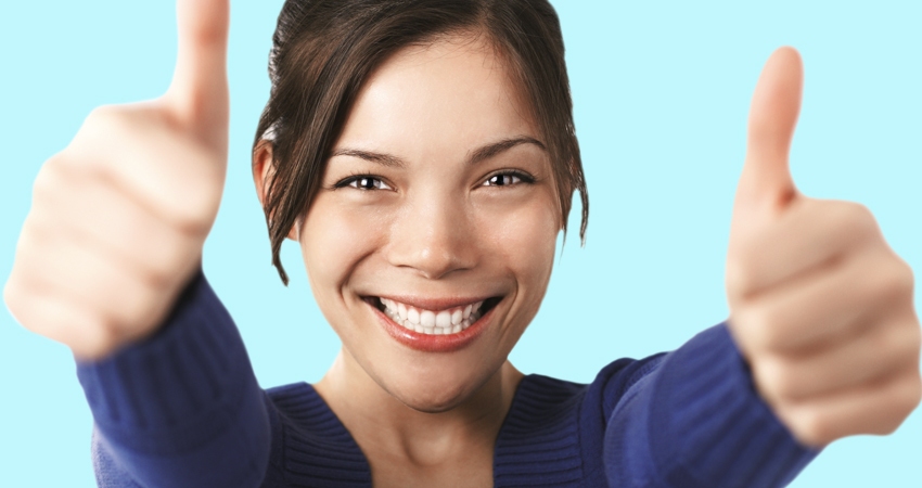 A girl smiles brightly while giving two thumbs up